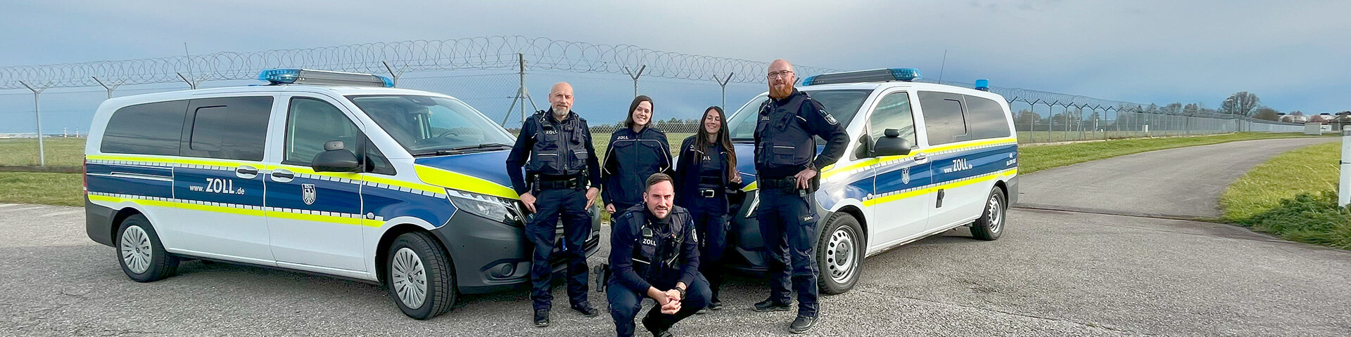 Gruppenbild von Zollbeamten:innen und Anwärter:innen mit 2 Einsatzfahrzeugen vor einem Grenzzaun | © Foto: GdP-Bezirksgruppe Zoll