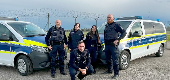 Gruppenbild von Zollbeamten:innen und Anwärter:innen mit 2 Einsatzfahrzeugen vor einem Grenzzaun | © Foto: GdP-Bezirksgruppe Zoll