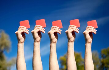 Hände von fünf Personen, welche jeweils eine rote Karte hochhalten. Die Szene findet unter freiem Himmel statt. | © Foto: AdobeStock #141076083 | Syda Productions