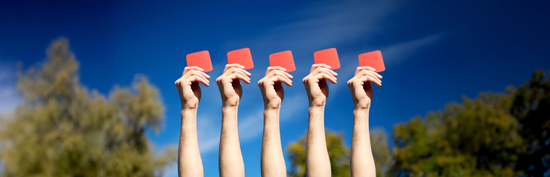Hände von fünf Personen, welche jeweils eine rote Karte hochhalten. Die Szene findet unter freiem Himmel statt. | © Foto: AdobeStock #141076083 | Syda Productions