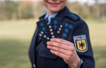Eine Frau in Polizeiuniform hält mehrere Abzeichen in der Hand in Richtung Kamera | © Foto: GdP-Direktionsgruppe Bundesbereitschaftspolizei