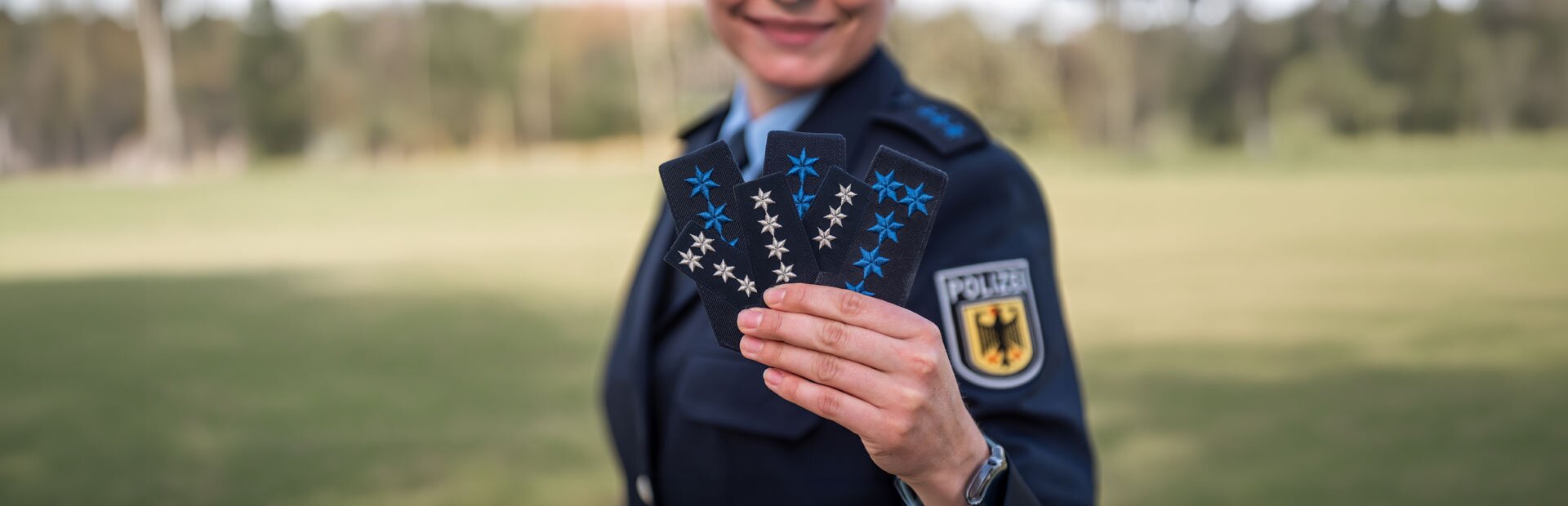 Eine Frau in Polizeiuniform hält mehrere Abzeichen in der Hand in Richtung Kamera | © Foto: GdP-Direktionsgruppe Bundesbereitschaftspolizei