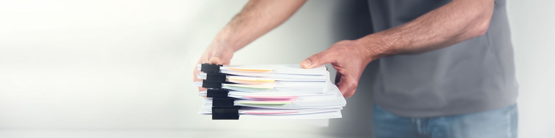 Ein Mann ist dabei, einen Pack gebündelter Unterlagen auf einen Tisch zu legen. | © Foto: AdobeStock #414536160 | ARAMYAN 