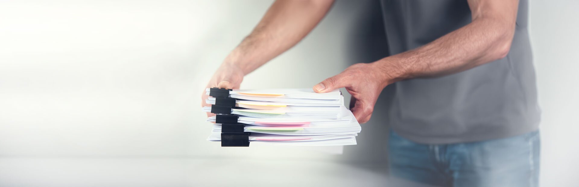 Ein Mann ist dabei, einen Pack gebündelter Unterlagen auf einen Tisch zu legen. | © Foto: AdobeStock #414536160 | ARAMYAN 