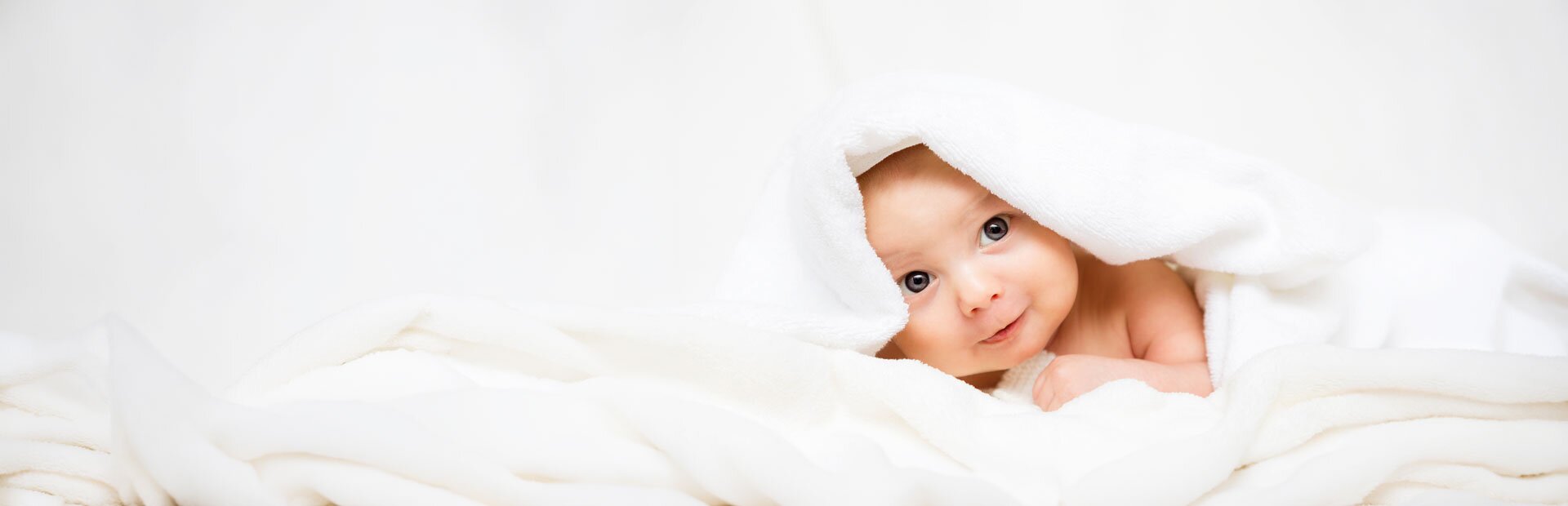Ein Baby mit blaugrauen Augen liegt in einem weichen Handtuch eingewickelt auf einem Tisch. | © Foto: AdobeStock #171484206 | ballabeyla