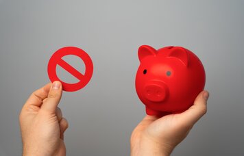 Rotes Sparschwein und Verbotsschild Nein in Händen auf grauem Hintergrund. | © Envato: iLixe48
